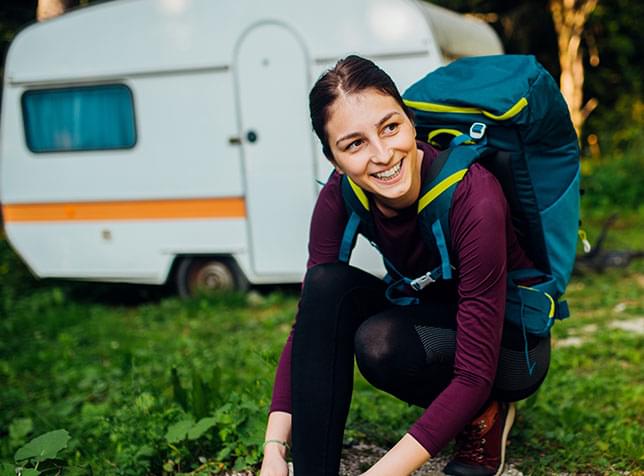Person with athletic clothing and equipment kneeling on grass outside travel trailer - link to The General Labs RV Insurance page